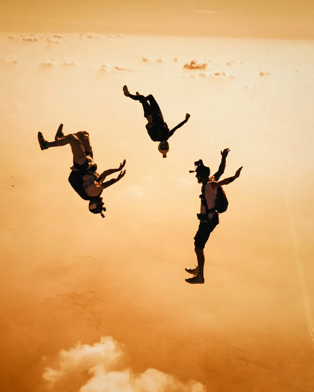 Skydivers in freefall against a saturated orange sunset