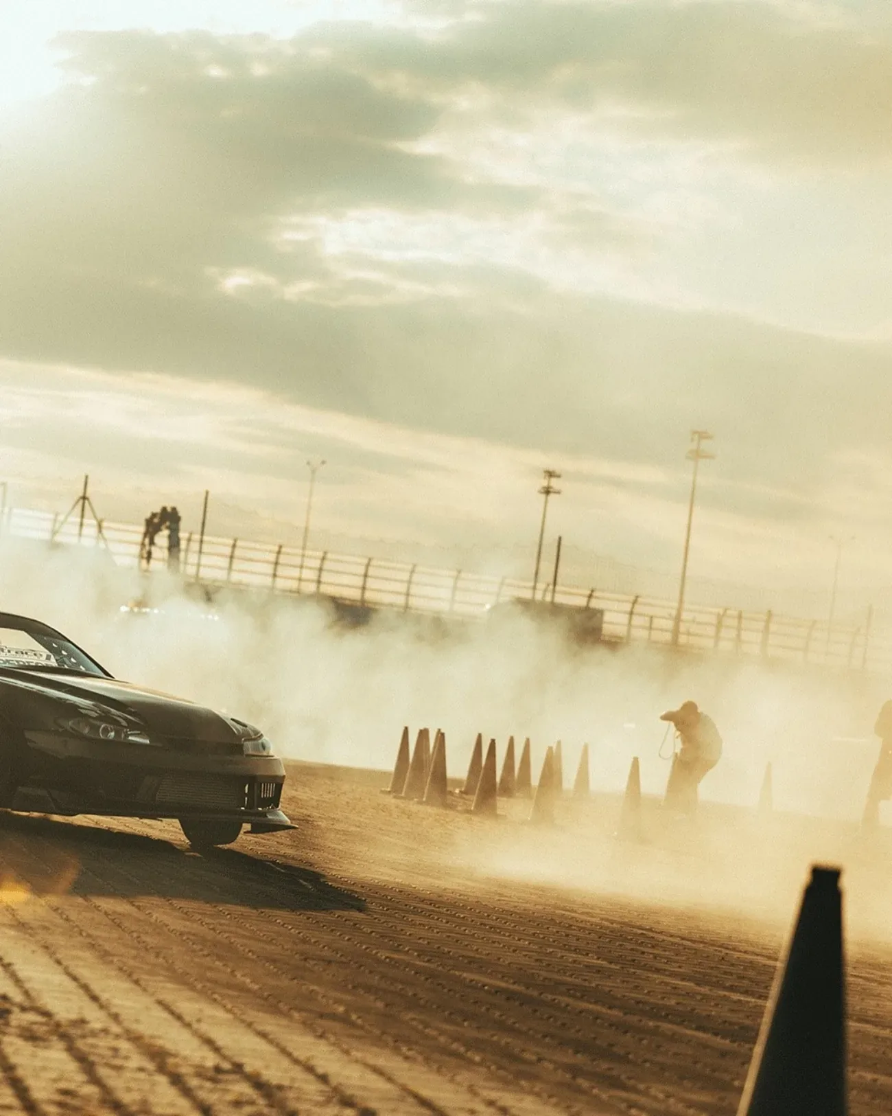 A drift car kicking up dust at golden hour during a stunt driving session